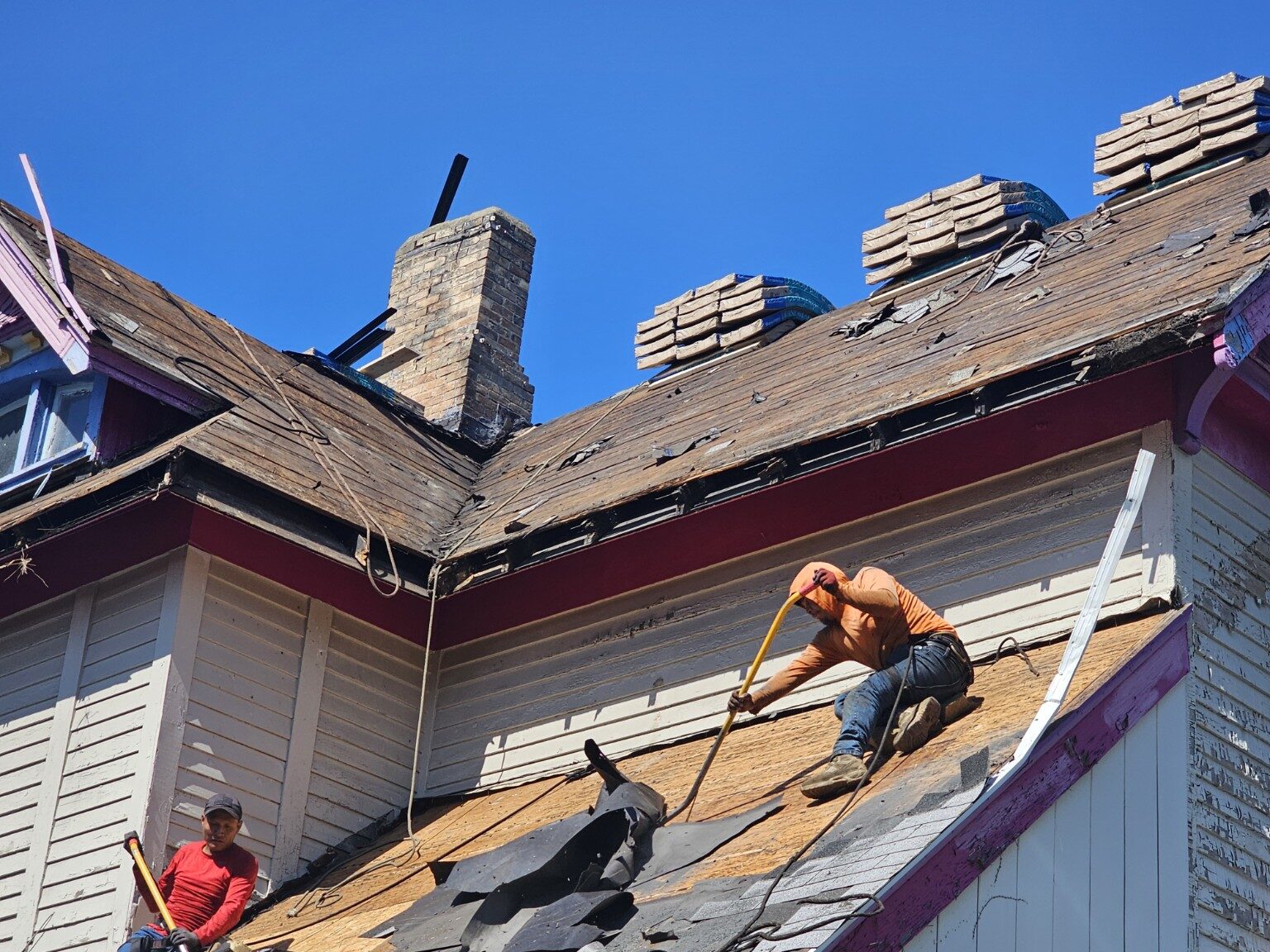 Crew installing new roofing around a chimney on a steep roof